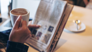 A business woman reading newspaper and drinking coffee in the morning in office